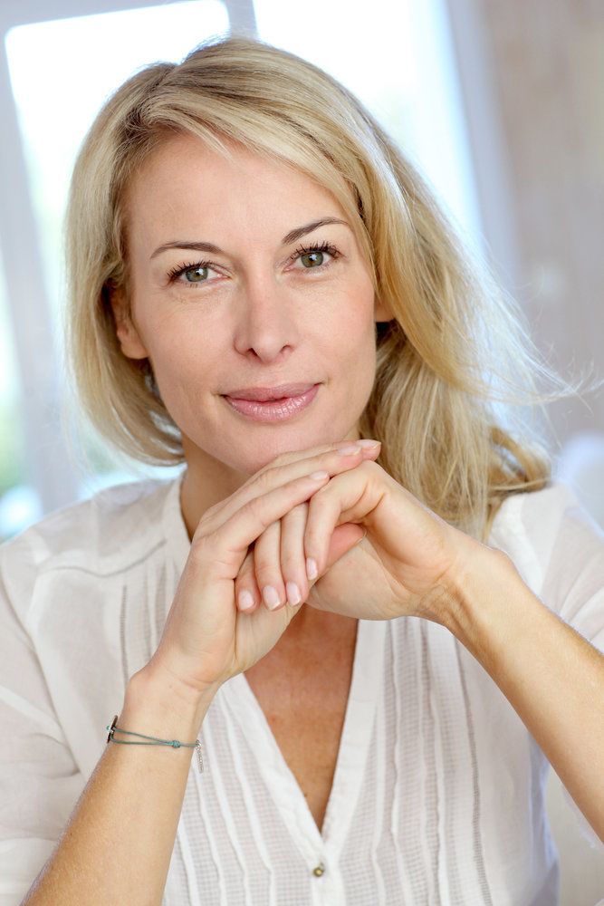 Middle-aged smiling blond woman resting chin on clasped hands